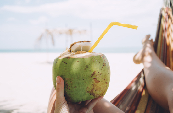 Hand Holding Coconut with Straw in it on sunny beach