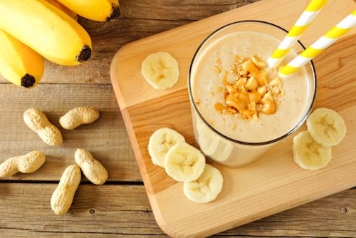 Smoothie au beurre d'arachide et à la banane dans un gobelet en verre avec une paille jaune
    